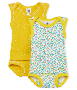 Un adorable bébé fille souriant, vêtu d'un body de danseuse à manches longues de la marque Petit Bateau, de couleur rose poudré. Le body met en valeur le confort et l'élégance du vêtement